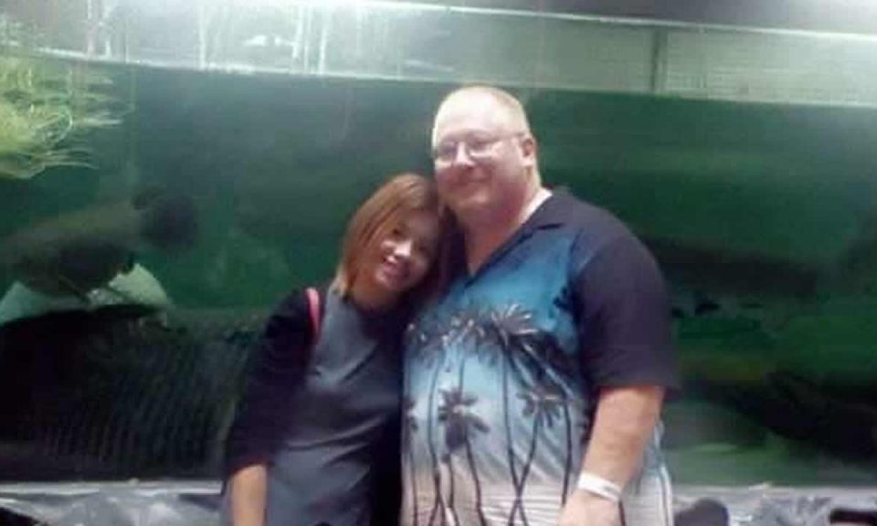 Holding The Line: Ann leaning on Charles and smiling in front of a large aquarium tank.